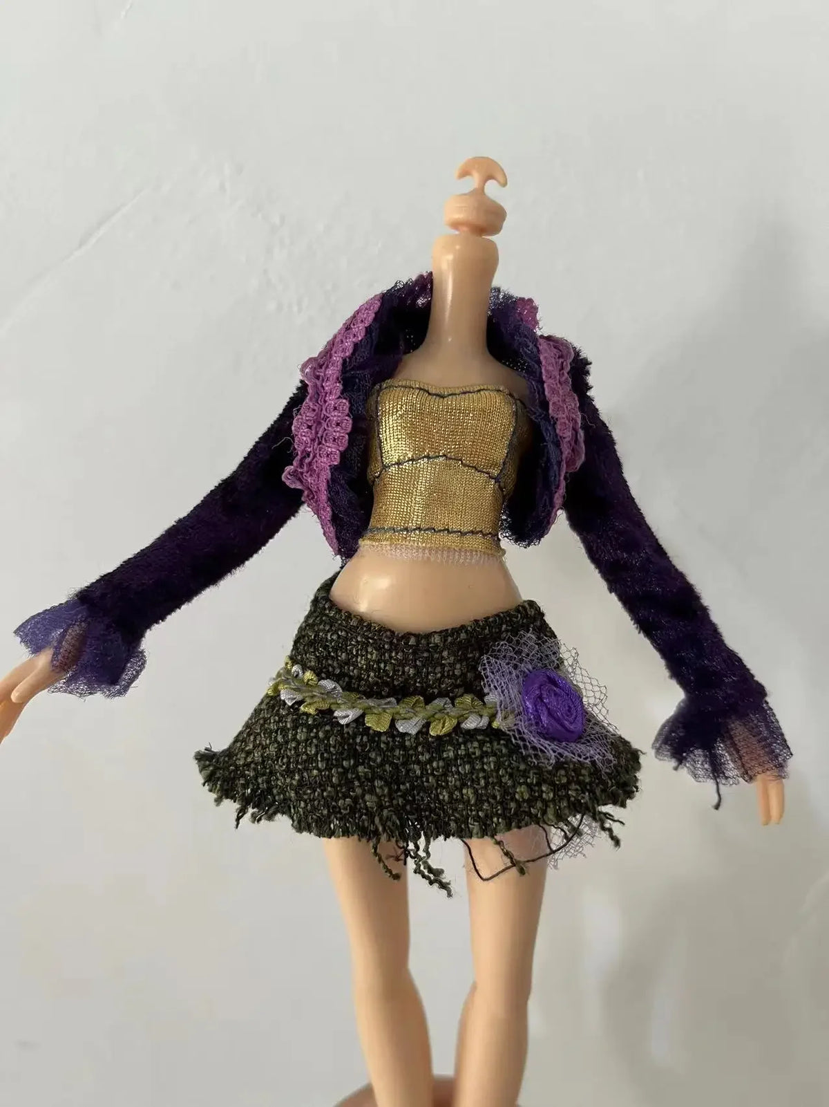 A fashion doll wearing a purple velvet jacket, gold top, and a dark green skirt with purple accents.