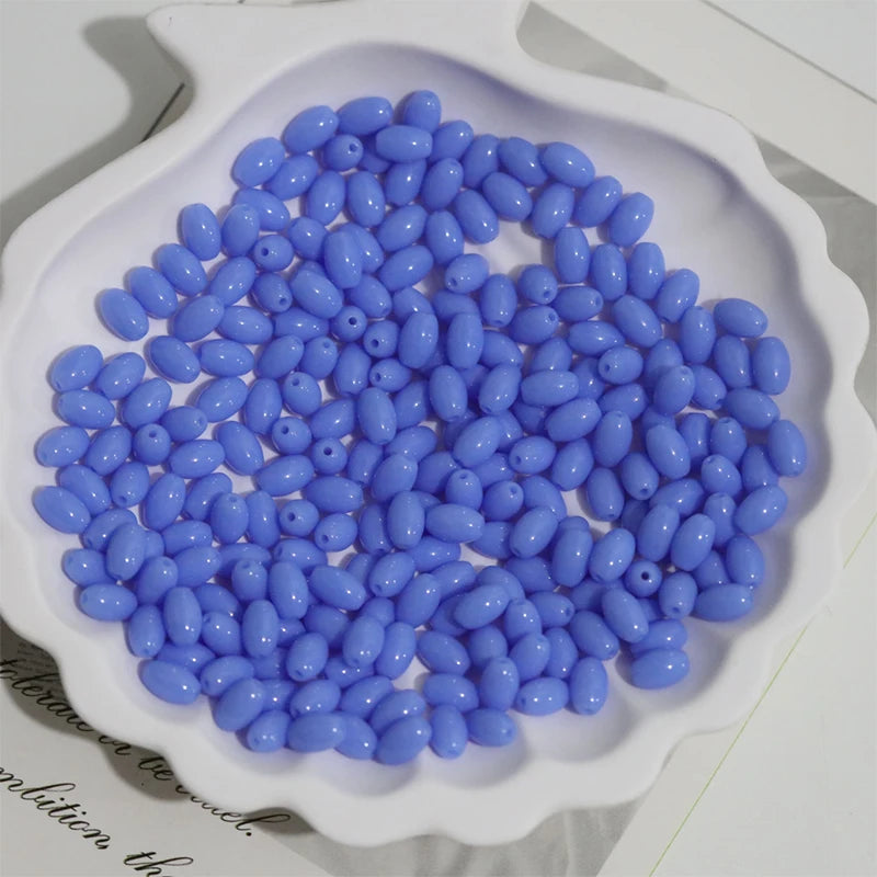 A pile of light blue oval glass rice grain beads for jewelry making displayed in a white dish.