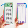 A hand holds a green multiplication flash card showing various 7 times tables, next to a purple flash card with a multiplicat