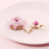 A pink crocheted donut fruit keychain pendant resting on a white plate.
