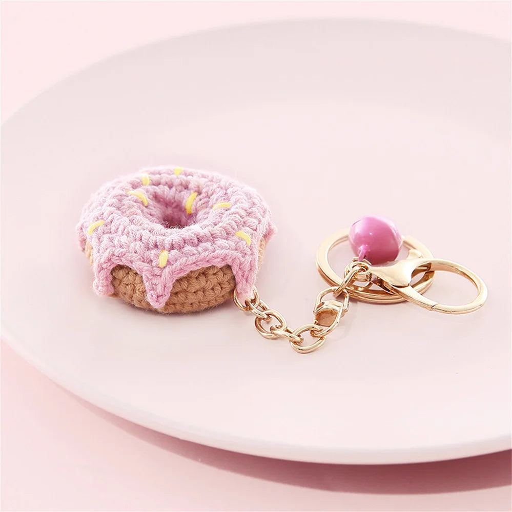 A pink crocheted donut fruit keychain pendant resting on a white plate.