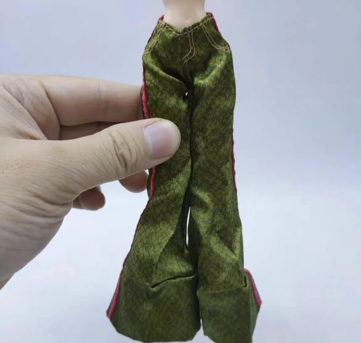 A hand holds a green fabric doll outfit for a fashion set.