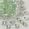 A pile of irregular square geometric glass beads in a pale green color scattered on a white surface.