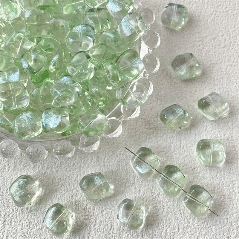 A pile of irregular square geometric glass beads in a pale green color scattered on a white surface.