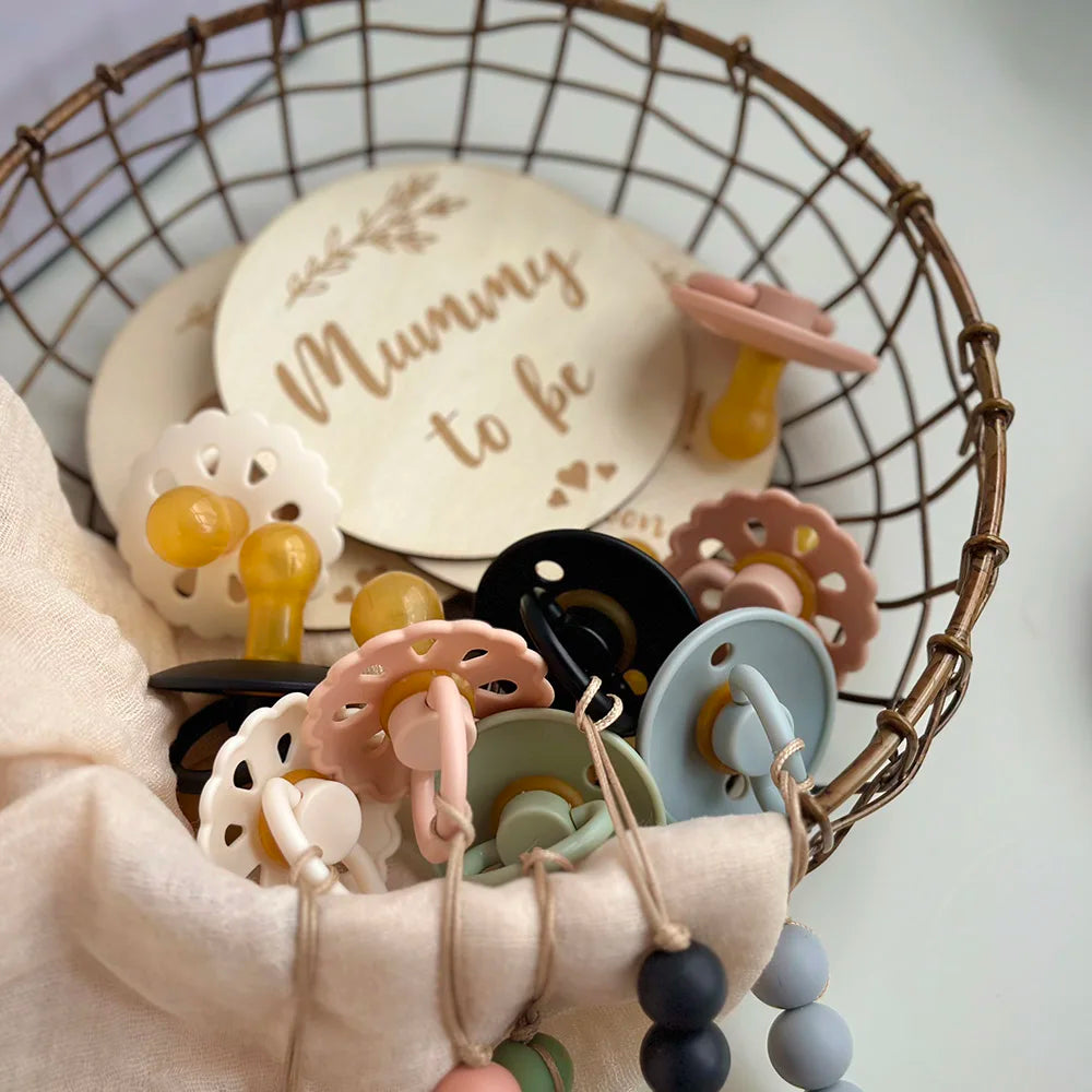 A collection of natural latex baby pacifiers in various pastel colors and shapes displayed in a woven basket.