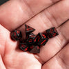A hand holds a set of black mini metal dice with red numbers and a bullet box for tabletop role-playing games
