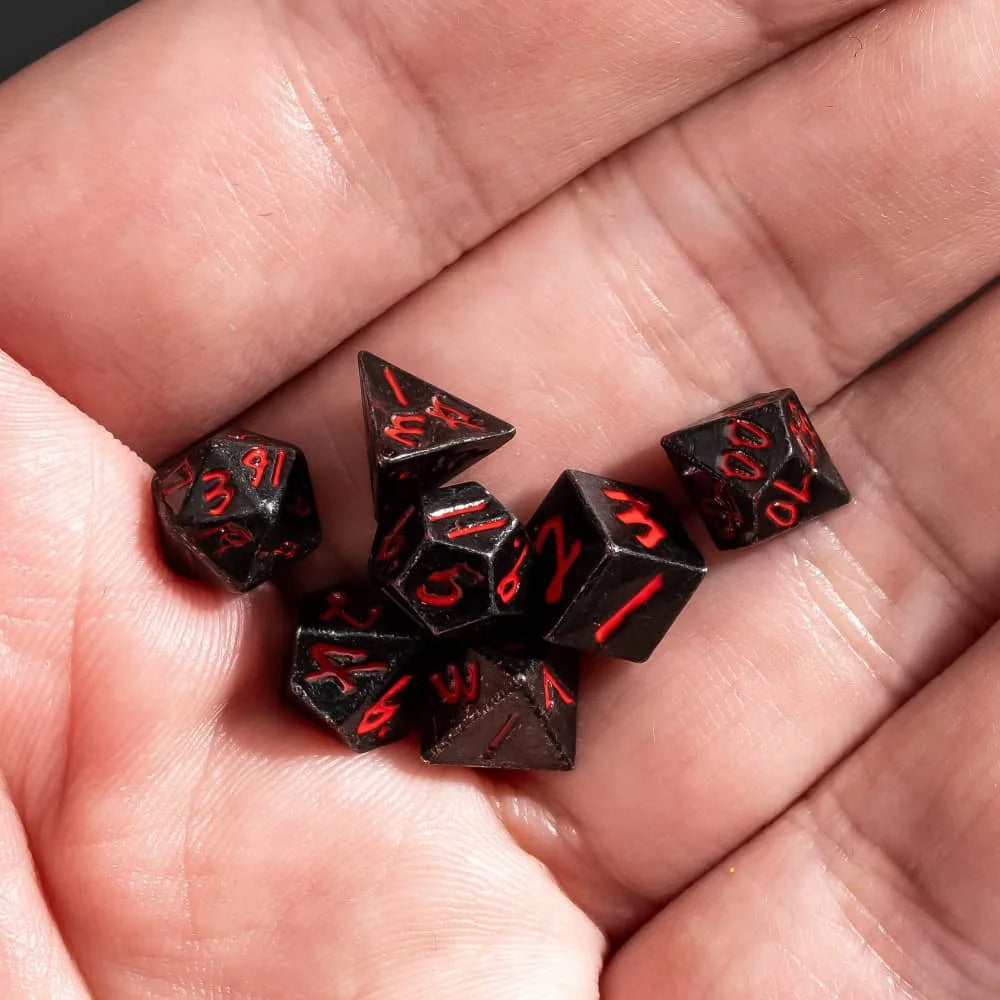 A hand holds a set of black mini metal dice with red numbers and a bullet box for tabletop role-playing games