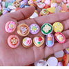 A hand holds a collection of colorful miniature dollhouse snack foods including candies and pastries.