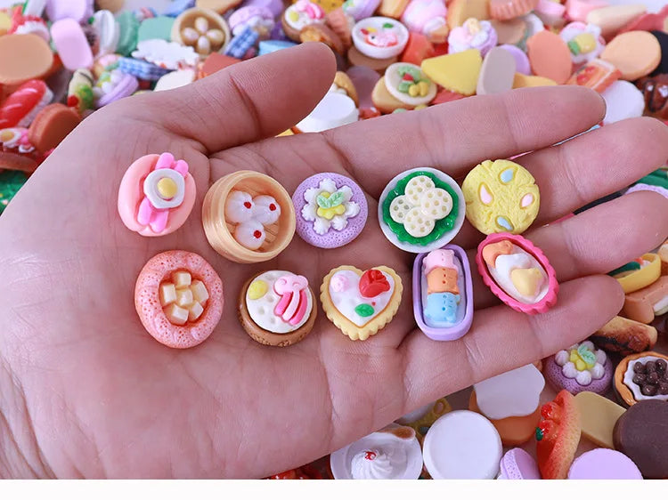 A hand holds a collection of colorful miniature dollhouse snack foods including candies and pastries.