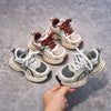 A hand holds a pair of red and white breathable mesh kids running sneakers with cushioned soles.
