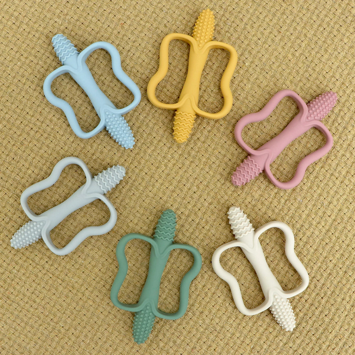 A collection of silicone teethers in various colors and shapes, including a yellow, light blue, pink, and white ones.