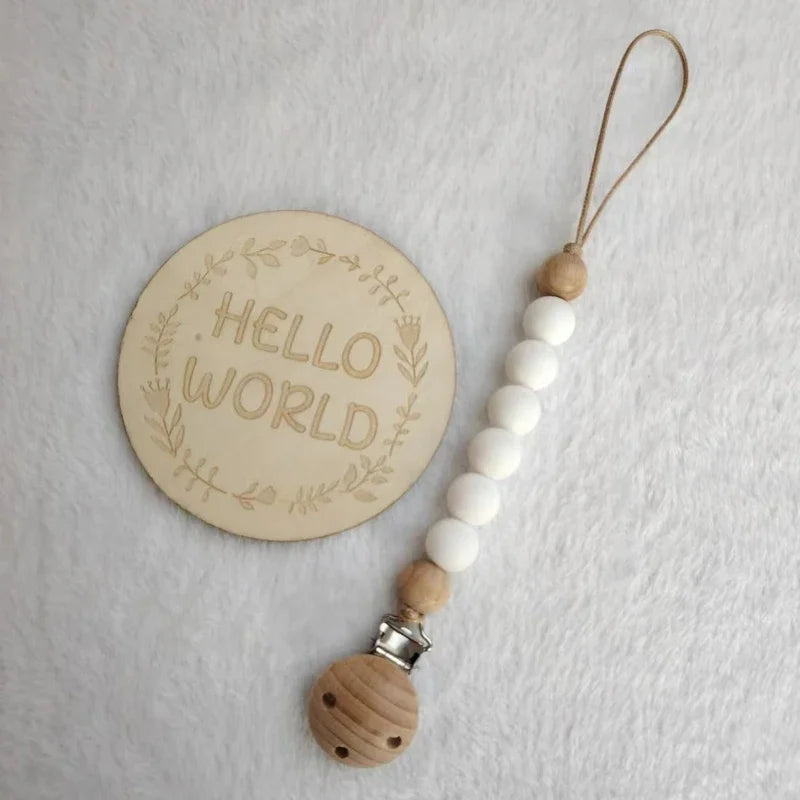 A wooden bead pacifier clip with silicone teether strung on a leather cord and attached to a round wooden disc.