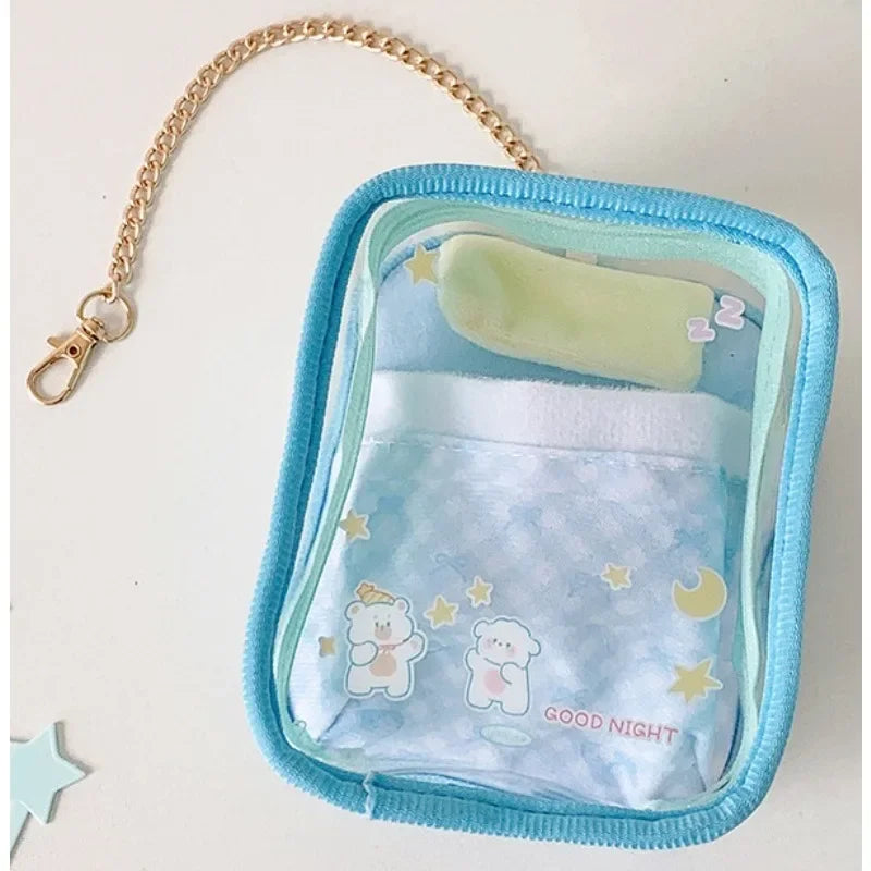 A light blue storage pouch with a clear plastic window and a gold chain keychain, containing soft fabric items for dolls.