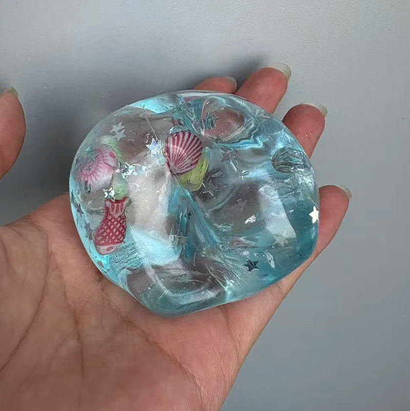 A hand holds a translucent blue sea glass or crystal block with internal inclusions like shells and stars.