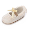A pair of light beige lace-trimmed baby girl moccasin shoes with a satin bow.