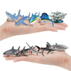 A hand holds a set of realistic mini ocean animal figurines including whales, sharks, dolphins, turtles, and penguins.