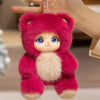 A pink plush pendant featuring a rabbit face with blue eyes and a fluffy texture, held by a hand.
