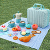 A blue wicker picnic basket set with teacups, pastries, and a teapot on a blue checkered cloth in green grass.