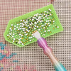 A green diamond painting mat holds a brush loaded with small, sparkling seed beads for crafting.