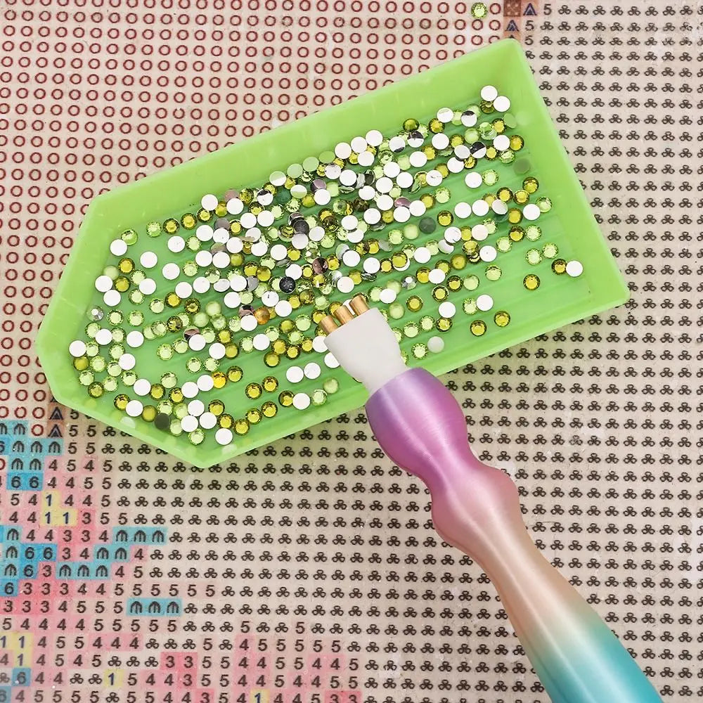 A green diamond painting mat holds a brush loaded with small, sparkling seed beads for crafting.