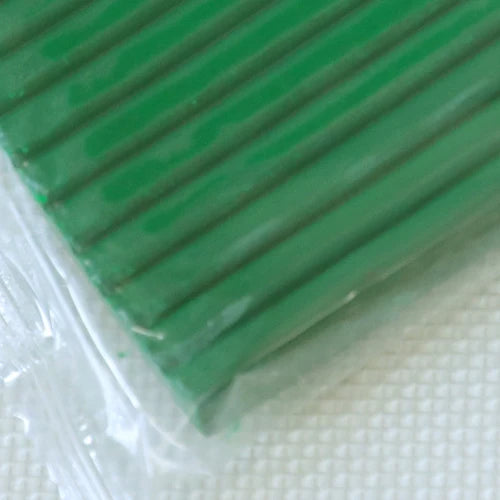 A close-up view of a green polymer clay kit with soft modeling clay visible beneath clear plastic packaging.