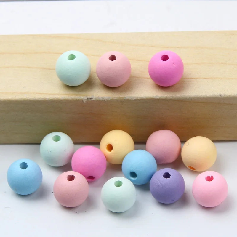 A collection of matte acrylic beads in various pastel colors including pink, blue, green, and yellow resting on a wooden surf