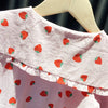A pink long-sleeve shirt for a baby girl with a strawberry print, displayed on a wooden hanger.