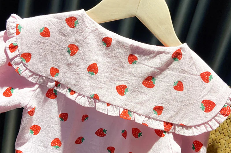 A pink long-sleeve shirt for a baby girl with a strawberry print, displayed on a wooden hanger.