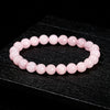 A bracelet made of small, round, pink quartz beads is displayed on a dark surface.