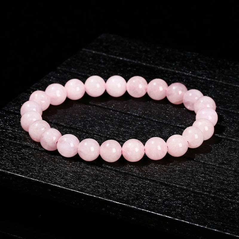 A bracelet made of small, round, pink quartz beads is displayed on a dark surface.