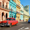 A red classic car is driving down a street lined with colorful historic buildings.