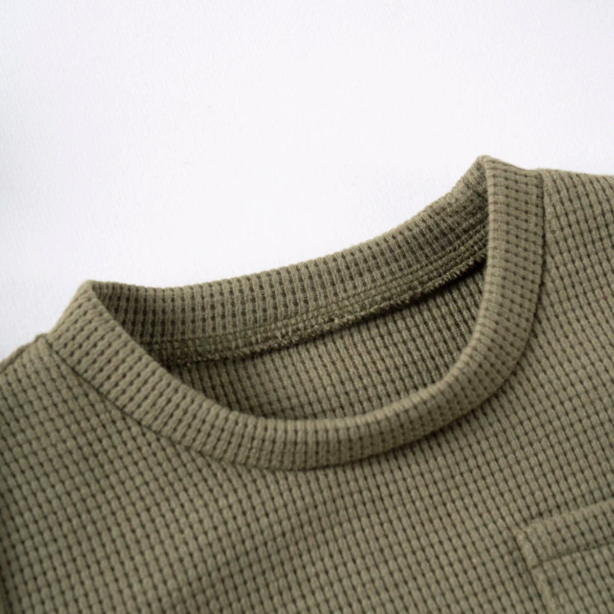 A close-up of a olive green knitted baby outfit set featuring a bear print tee and shorts.