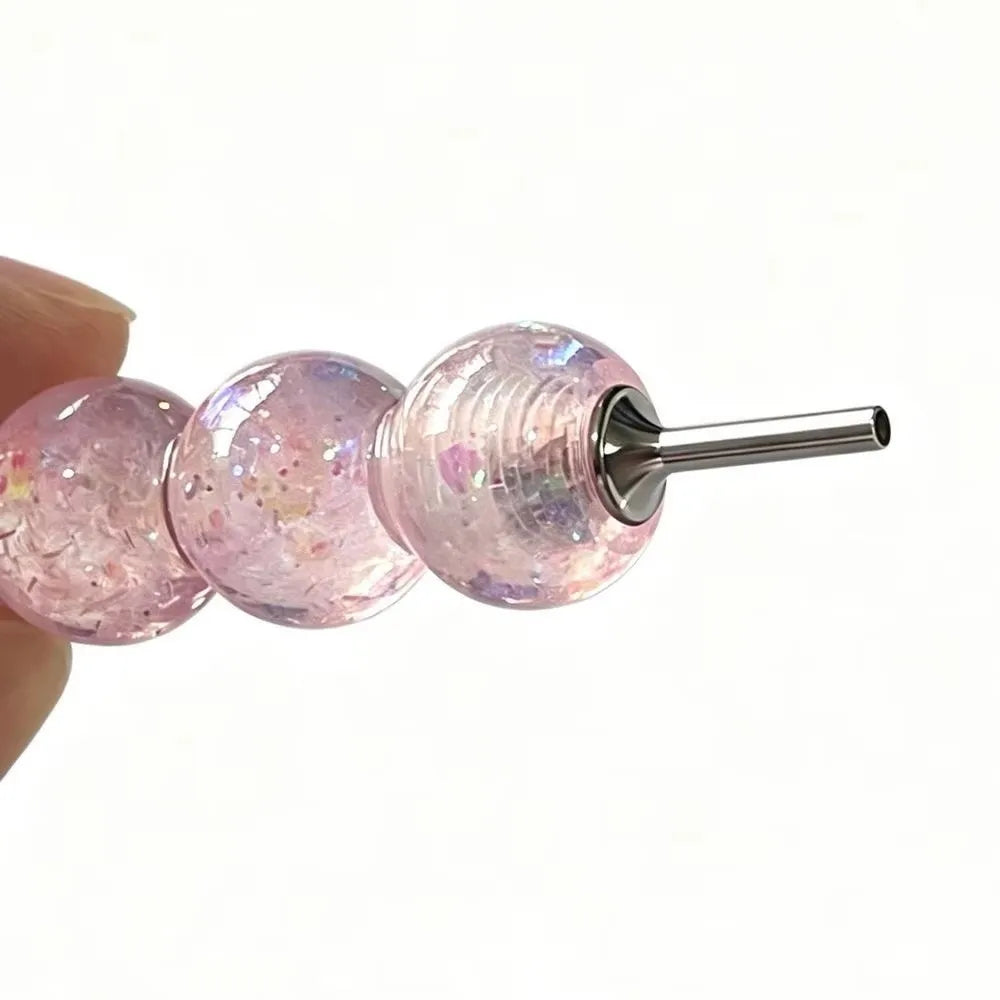 A pink glass painting pen tip with a metal shaft and three round glass beads on a finger.