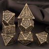A set of seven antique metal polyhedral dice, including a pyramid and dodecahedron shape, resting on dark fabric.