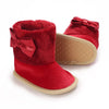 A pair of red velvet baby first walker shoes with bow accents and tan soles.