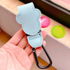 A hand holds a light blue PU leather stroller organizer hook with a black clip and a bright green button.