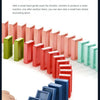 A hand is pushing a train of colorful domino blocks across a white surface.