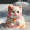 Jouet en peluche chat orange et blanc avec des marques rouges, assis sur une surface blanche.