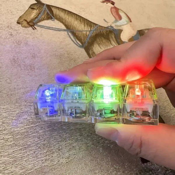 A hand holds several clear mechanical keyboard keychain fidget toys emitting various colored lights.