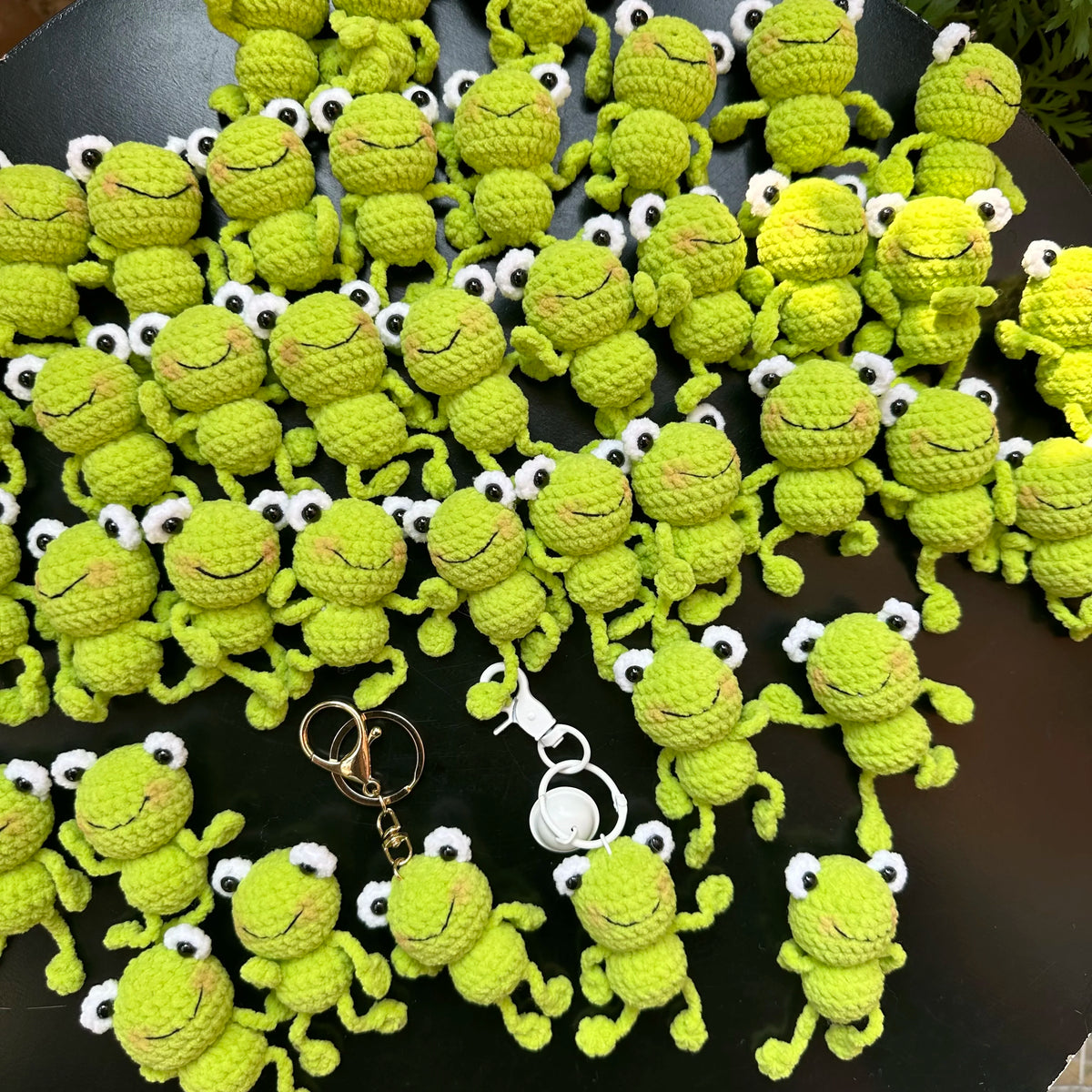 A large collection of handmade crochet frog keychains in various shades of lime green and yellow.