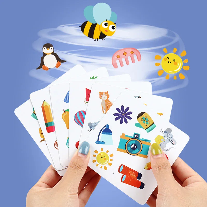 Hands hold a deck of Animal Memory Match Cards featuring bees, penguins, and various colorful objects against a light blue ba
