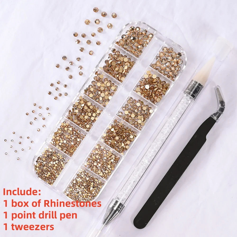 A box of gold rhinestones, a point drill pen, and tweezers are displayed on white paper.