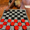 A child is playing a game on a black and white checkered rug with red plastic pieces.