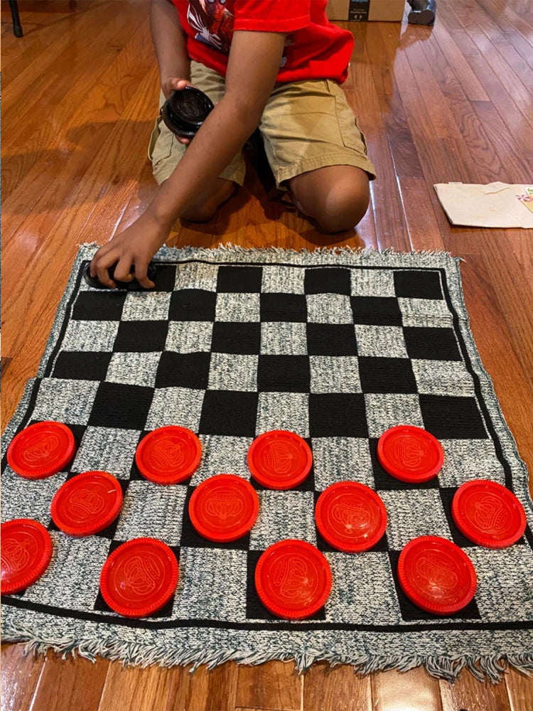 A child is playing a game on a black and white checkered rug with red plastic pieces.