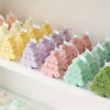 A row of silicone Christmas tree shaped cookie and candle molds in various pastel colors displayed on a white shelf.