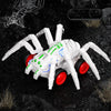 A white inertia-powered spider crawling toy car with red wheels is shown on a dark, rocky surface.