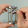 A hand holds a multi-layer stainless steel puzzle cage brain teaser with spiky metal rods inside.