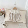 A beige sleeveless cotton jumpsuit for a baby girl with a delicate lace collar hanging on a hanger.