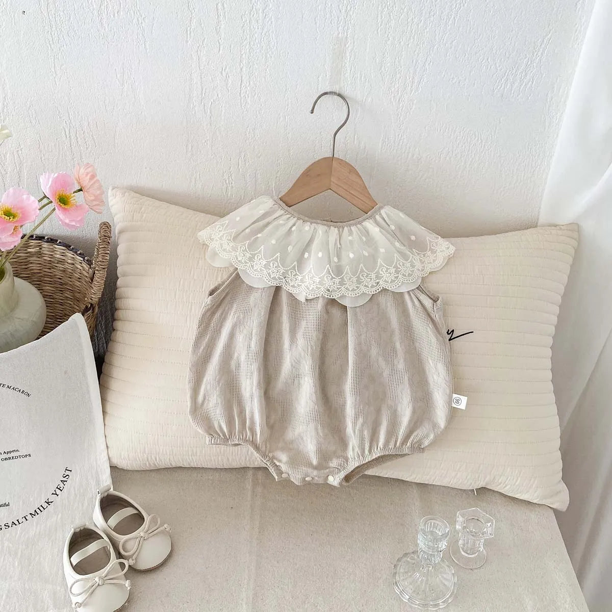 A beige sleeveless cotton jumpsuit for a baby girl with a delicate lace collar hanging on a hanger.