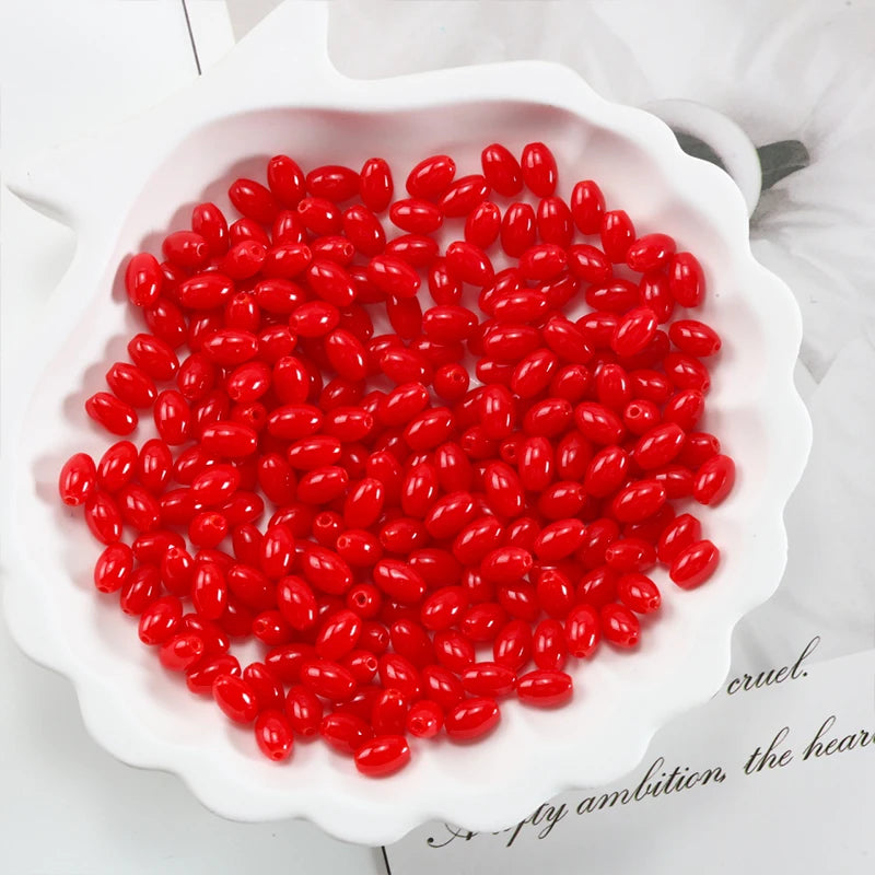 A pile of bright red oval glass rice grain beads for jewelry making in a white dish.